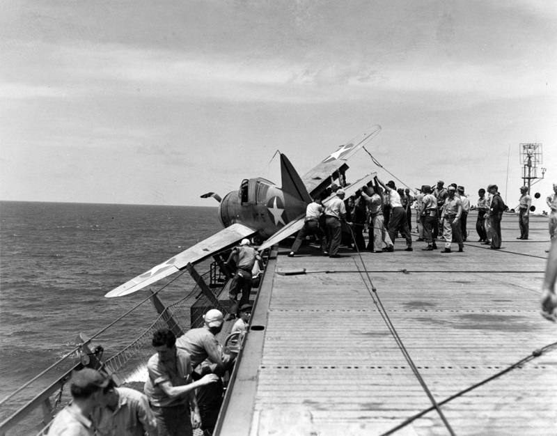 Brewster F2A-3 "Buffalo" fighter, of Marine Fighting Squadron 211 (VMF-211) Rests in the flight deck gallery netting after suffering landing gear failure while landing on board USS Long Island (AVG-1) off Palmyra Island, 25 July 1942. Note marking "MF-5" on the plane's fuselage and very weathered paint. The carrier's SC radar antenna is visible atop her stub mast at right (Photo: U.S. Navy)